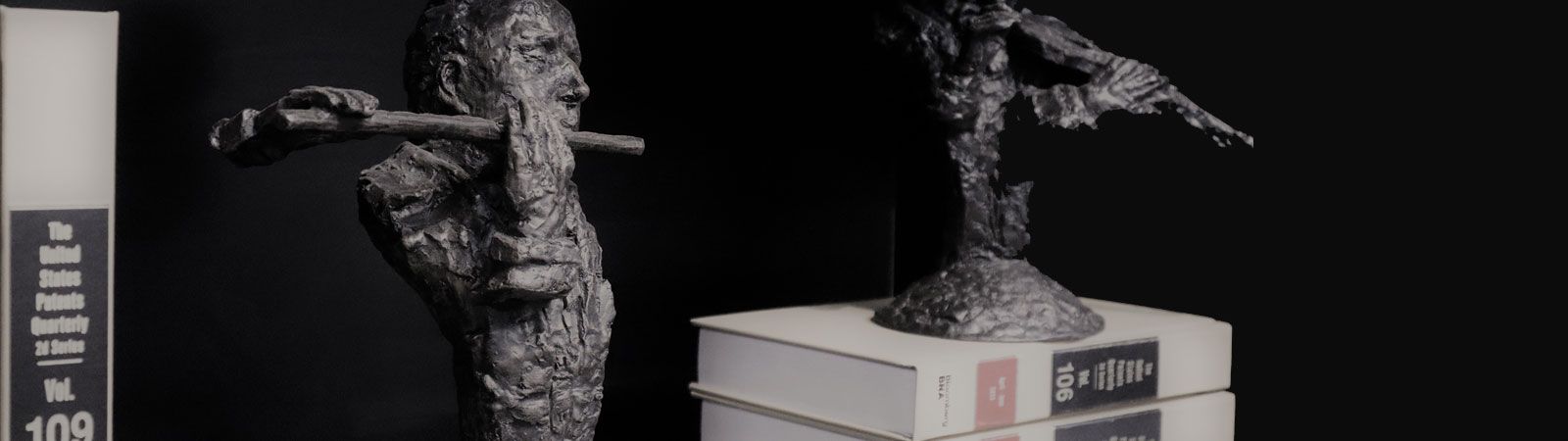 Sculptures beside United States Patents Quarterly volumes on a black background